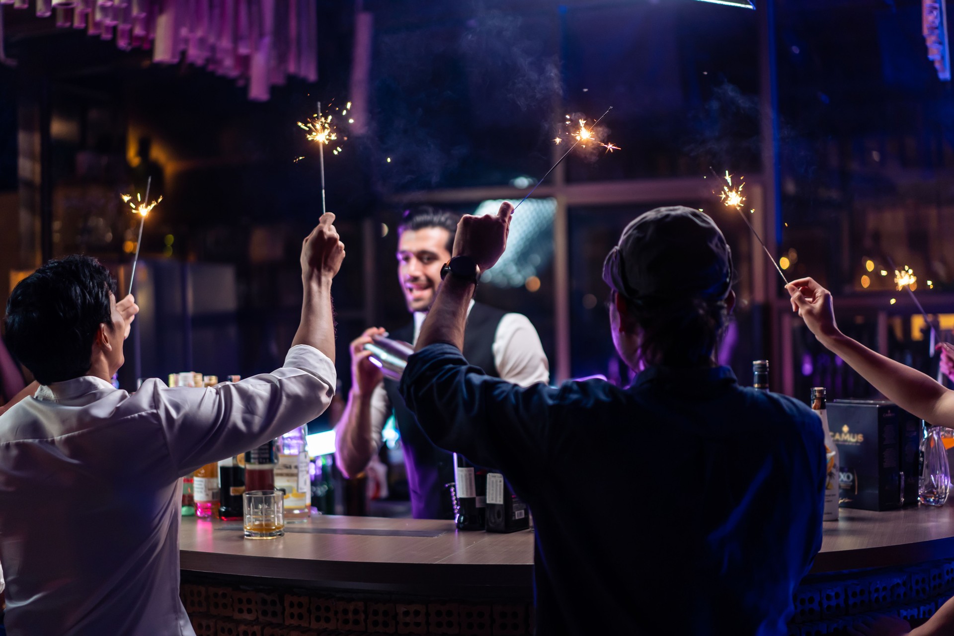 Caucasian profession bartender making a cocktail for young men at a bar. Attractive barman pouring mixes liquor ingredients cocktail drink from cocktail shaker into the glass at night club restaurant.