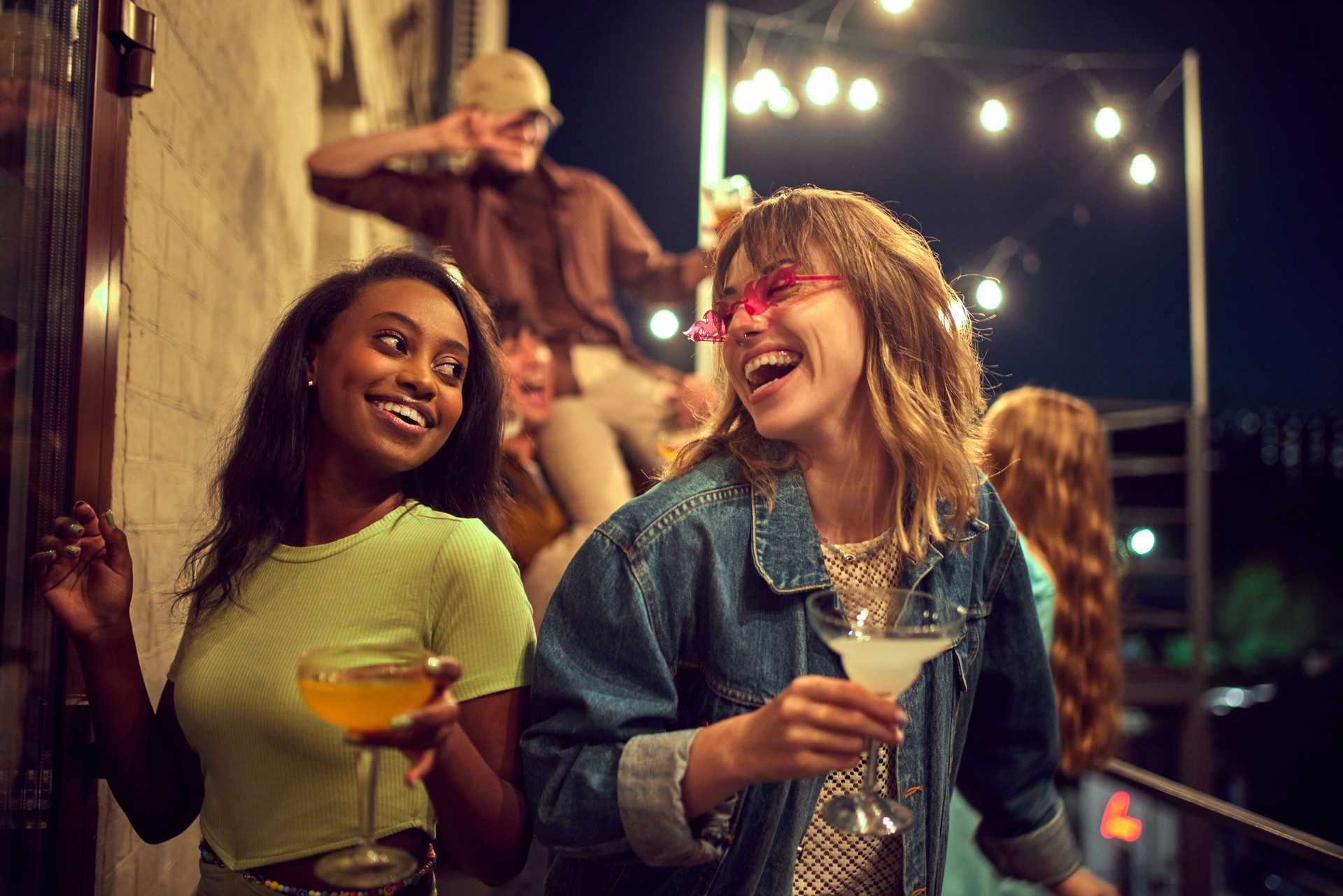 Cheerful, positive, happy young people, friends meeting outdoors, in cafe, having fun and drinking cocktails